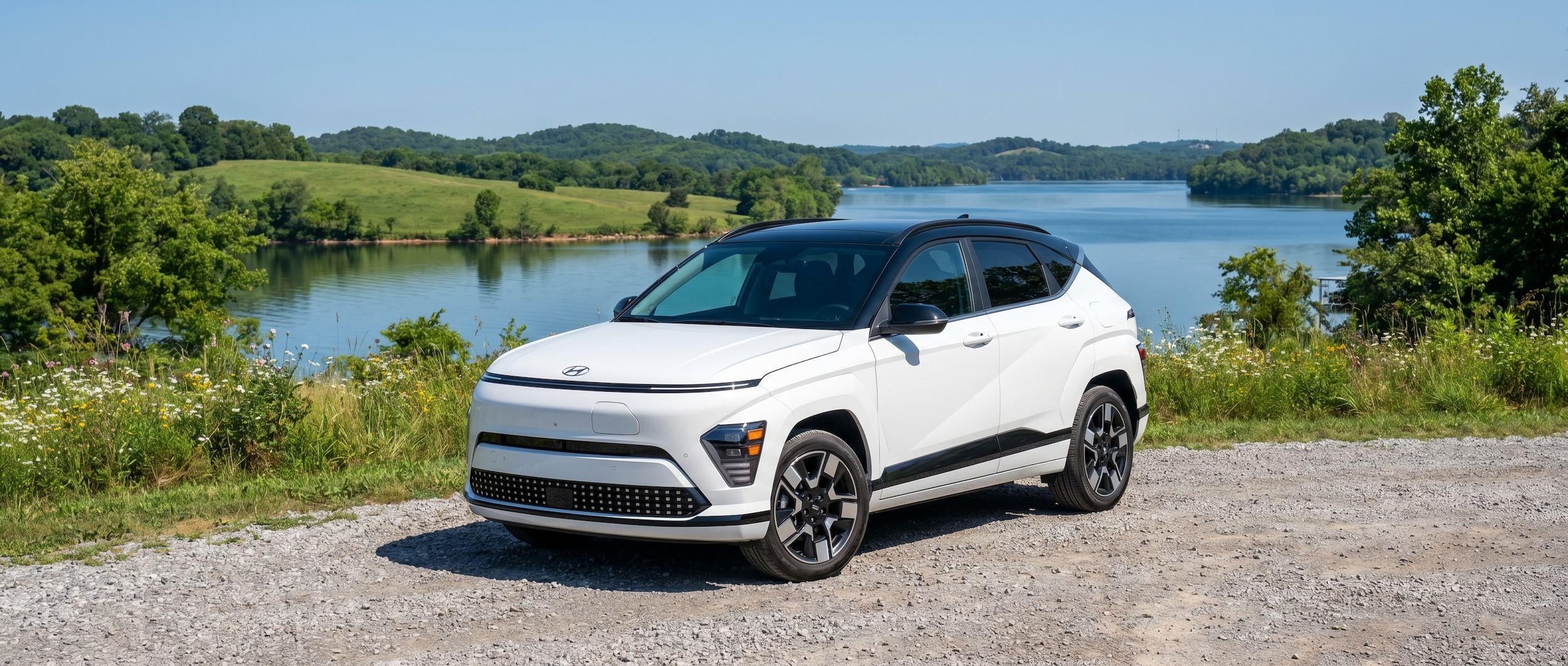 A vibrant Hyundai Kona Electric parked near a scenic lakeside overlook in Hendersonville, Tennessee, with lush green hills and calm water visible in the background on a clear sunny day.
