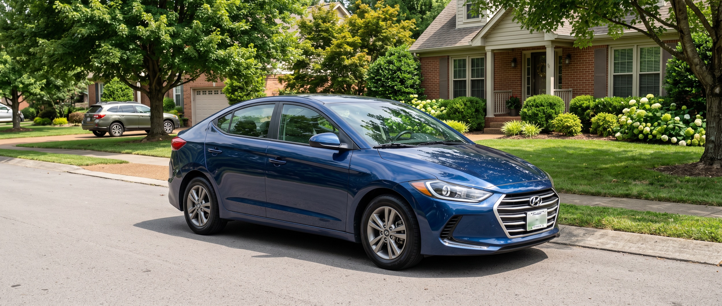 A clean used Hyundai Elantra in a silver or dark blue finish parked in a suburban Nashville-area neighborhood in August sunlight, with lush summer foliage in the background, evoking a back-to-school purchase for a Middle Tennessee commuter