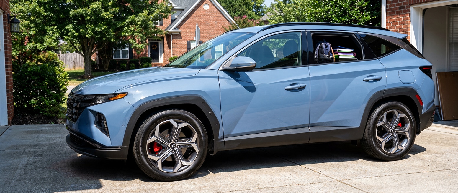 A 2026 Hyundai Tucson parked in a suburban Hendersonville, TN driveway on a bright August morning, front wheel facing forward with brake caliper faintly visible through the wheel spoke, school supplies visible in the back seat through the rear window