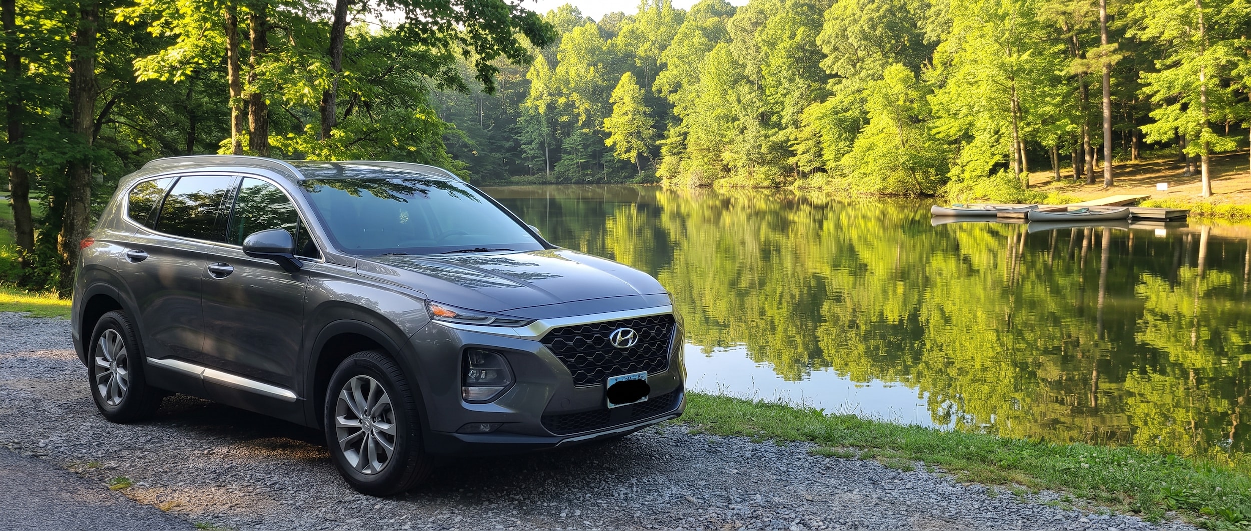 A clean Hyundai SUV parked near a lakeshore on a bright summer morning in Tennessee, with green trees reflecting on calm water in the background, sunlight filtering through the leaves.