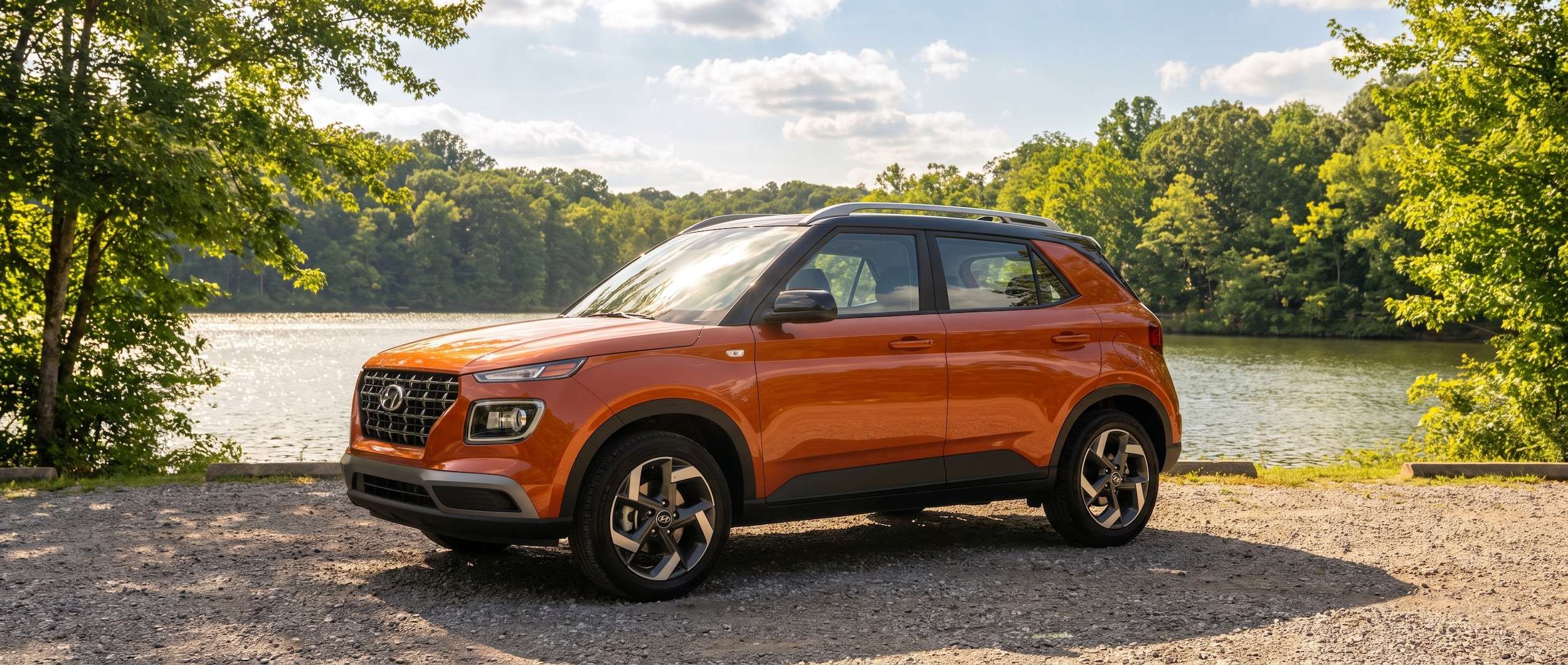 A 2026 Hyundai Venue in a bold two-tone color parked at a lakeside park in summer, green trees and shimmering Tennessee lake water in the background, late-morning golden light, blue sky with scattered clouds