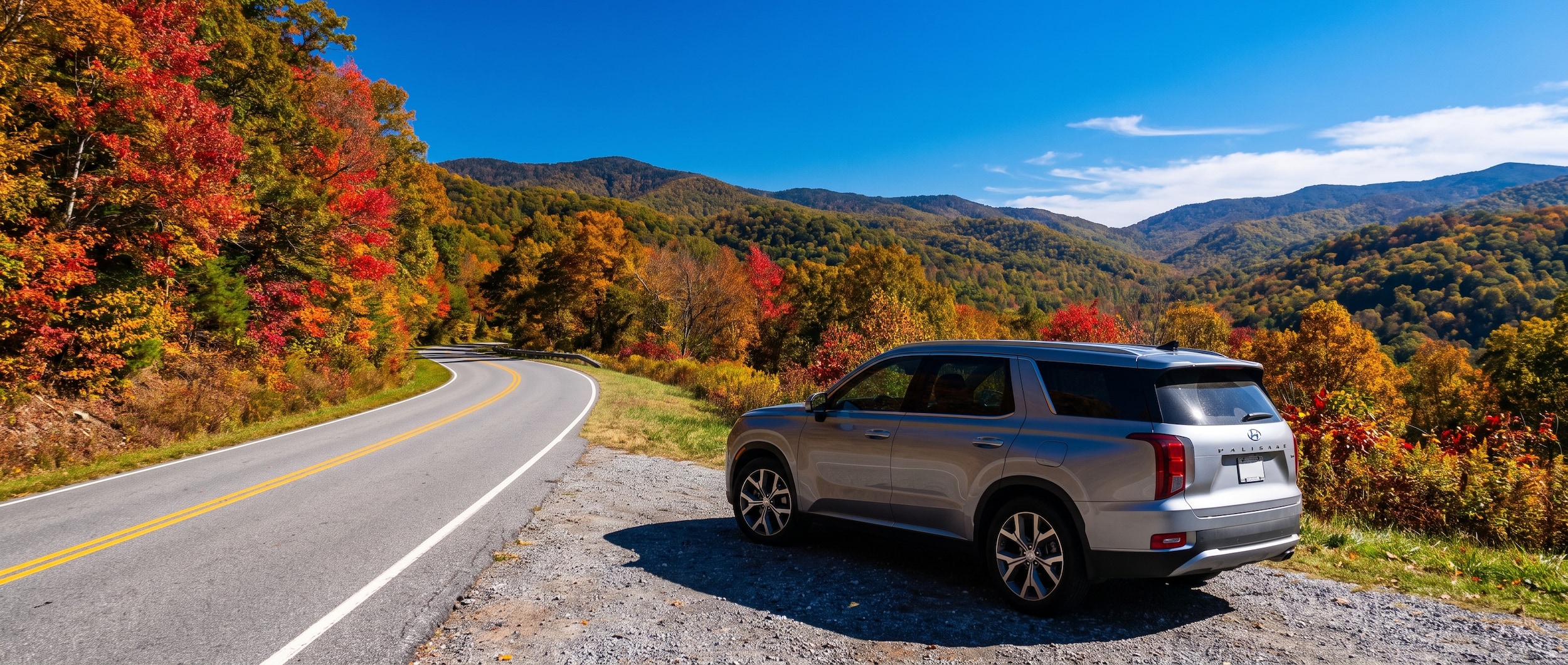 A silver Hyundai SUV parked along a scenic Tennessee highway lined with autumn trees, with rolling green hills visible in the background and a clear blue sky overhead.