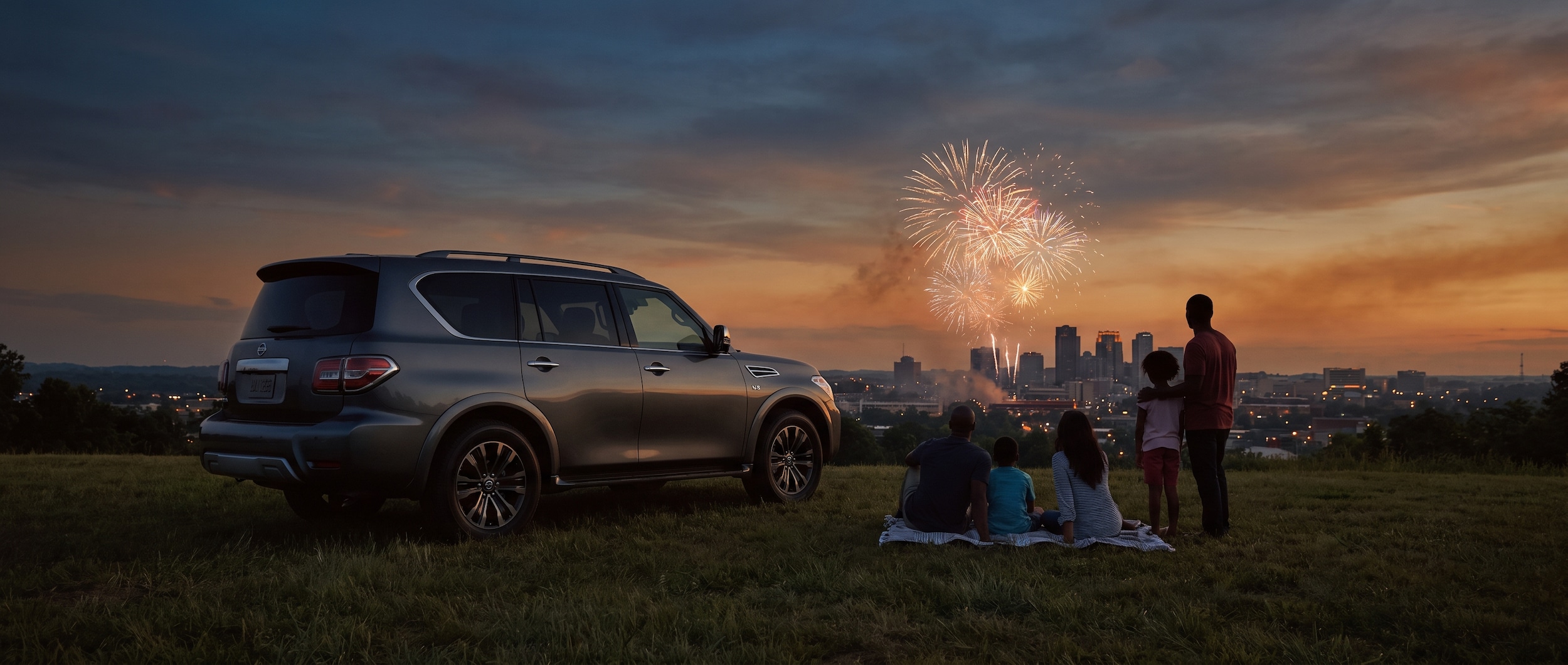 Nissan Armada parked near Birmingham July 4th fireworks at dusk with city skyline in background