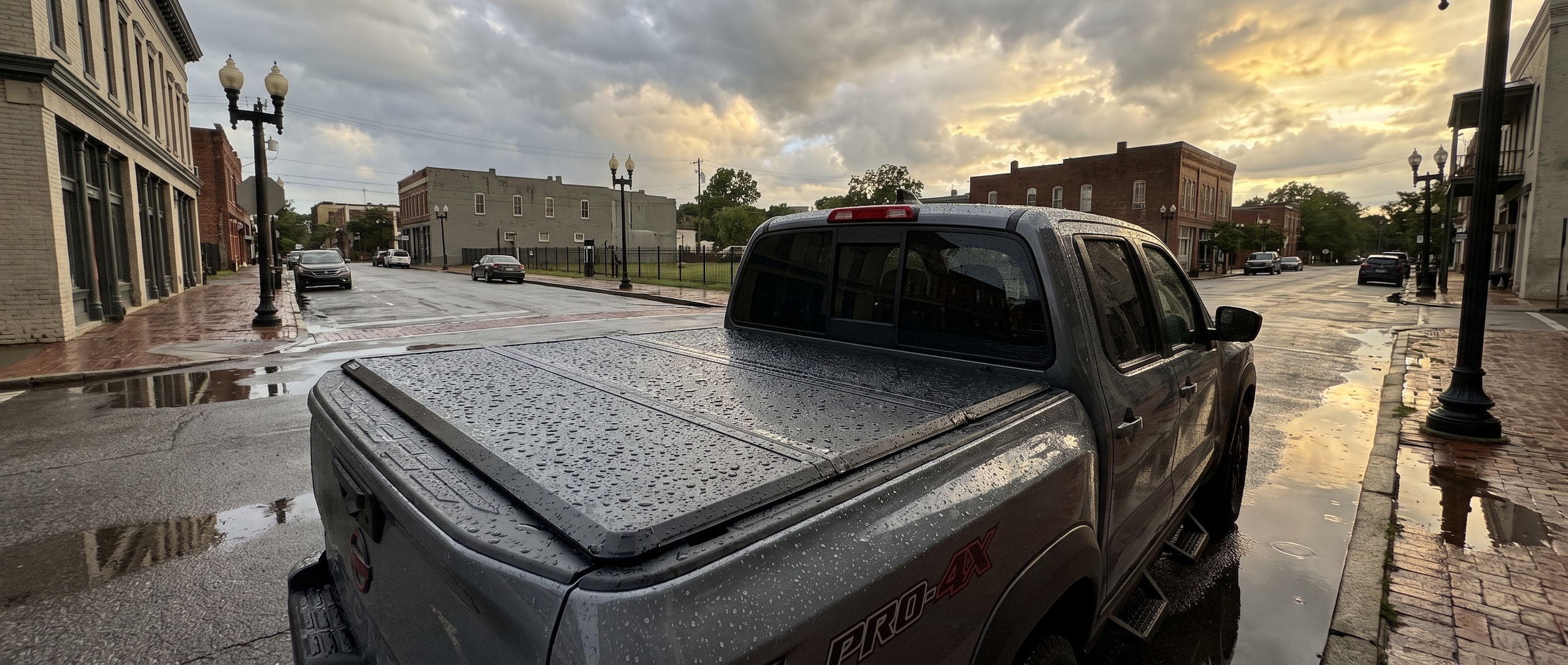 2026 Nissan Frontier with black hard tri-fold tonneau cover on a wet Birmingham street after summer rain
