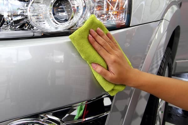 Person with a lime green cleaning cloth polishing the front bumper of a new car