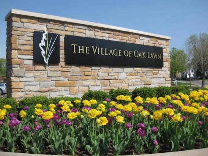 Sign stating The Village of Oak Lawn, welcoming visitors, surrounded by landscaped yellow and purple summer flowers, sourced from OakLawn-IL.gov