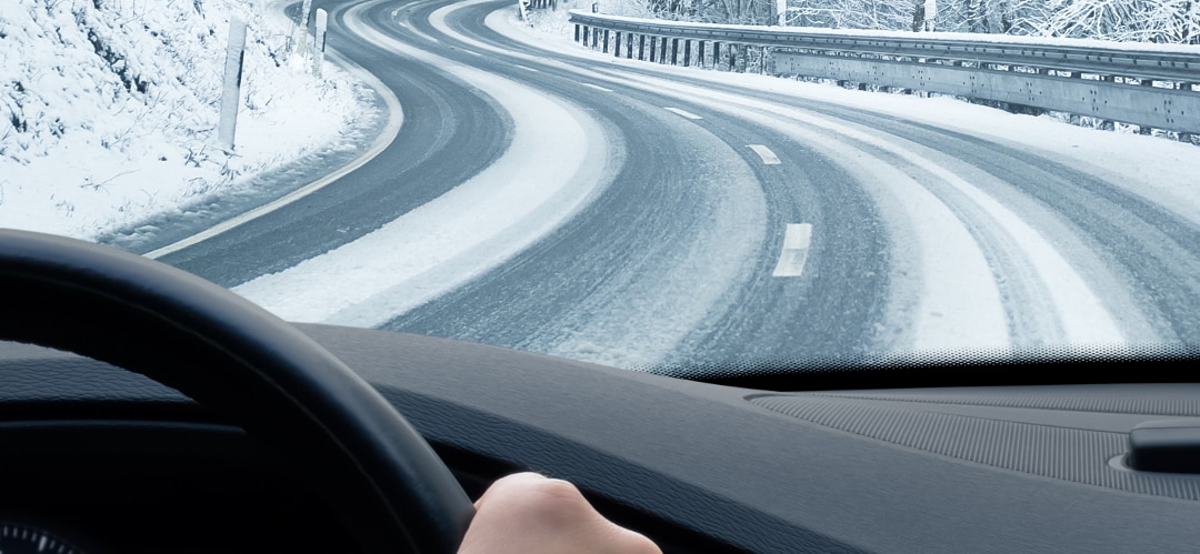 person behind steering wheel of car driving along snowy road