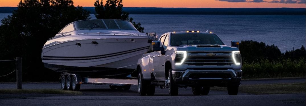 White 2024 Chevy Silverado HD Towing a Boat at Twilight