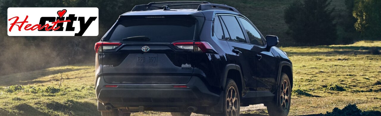 A black Toyota RAV4 Hybrid is driving on a dirt road through a lush green field.