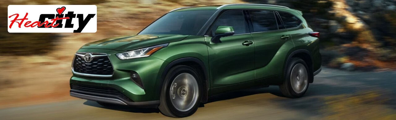 A green 2024 Toyota Highlander driving on a winding road.