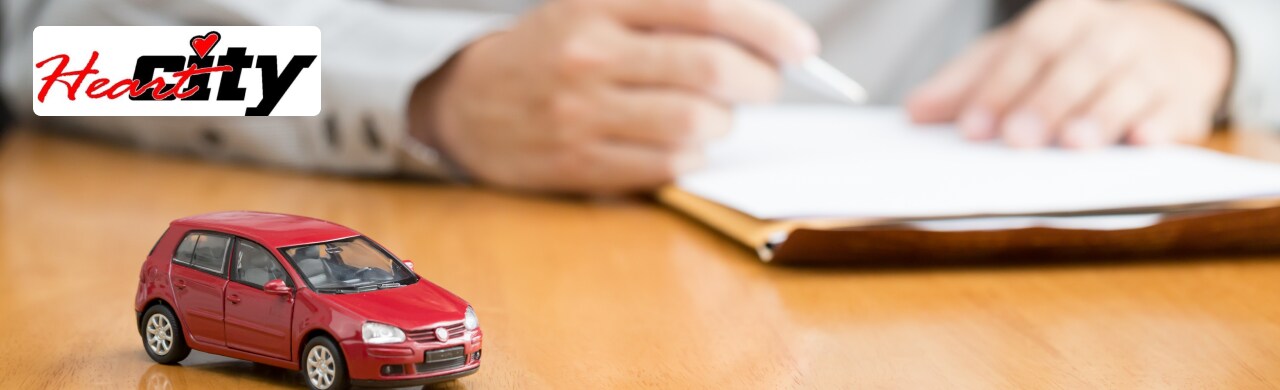 A red toy car sits on a table in front of a person signing paperwork.