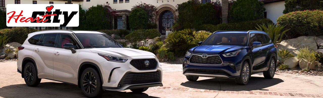 A white and a blue 2024 Toyota Highlander parked in front of a house.