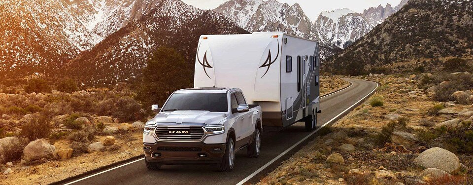 2019 Ram 1500 A white 2019 Ram 1500 towing a trailer down an open road