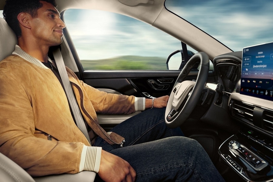 A person is shown using Lincoln BlueCruise hands-free highway driving technology on a divided highway called a Hands-Free Blue Zone.
