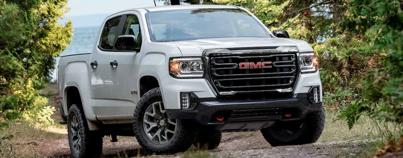 A white 2022 GMC Canyon is shown parked on a dirt trail lined with trees.