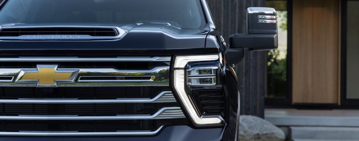 A close up shows the grille and driver side headlight on a black 2024 Chevy Silverado 2500HD High Country.