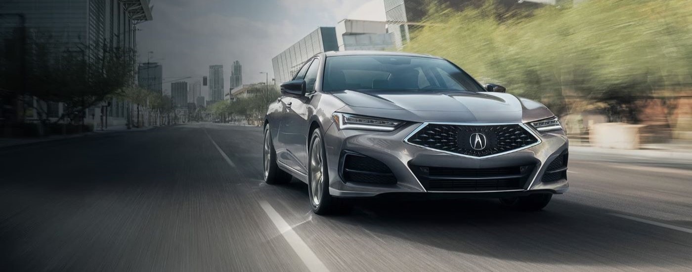 A silver 2023 Acura TLX is shown driving on a city street.