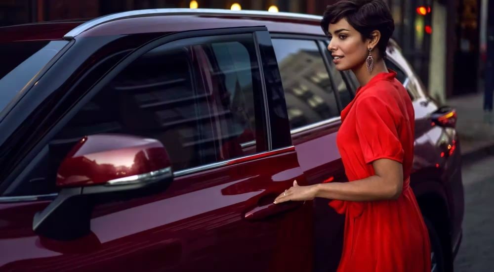 A person is shown opening the door on a maroon 2023 Toyota Highlander Hybrid Platinum.