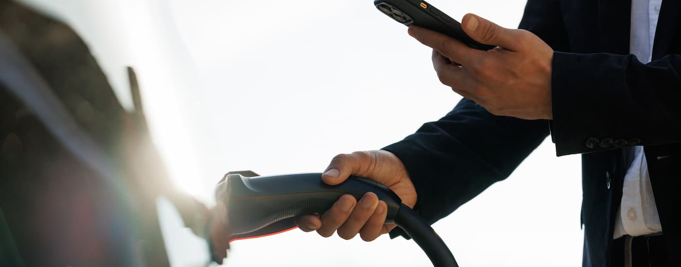 Electric Vehicles for Sale - Plugged IN.jpg A hand is shown plugging a white EV vehicle into a charging station.