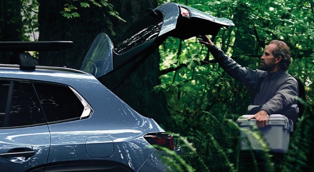 A person is shown stowing a cooler in a blue 2023 Mazda CX-50.