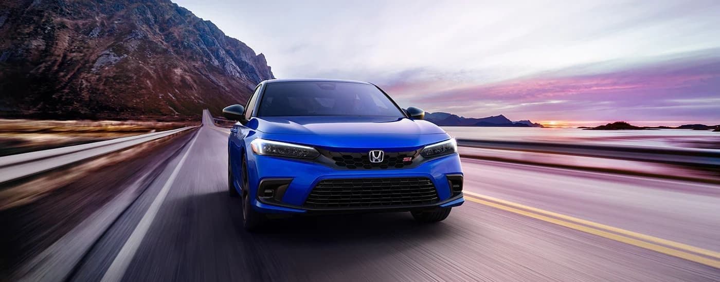 A blue 2023 Honda Civic Si is shown on a coastal road at sunrise.