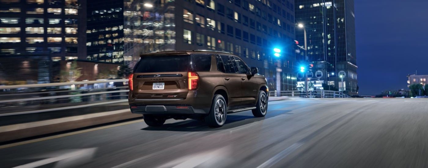 A brown 2022 Chevy Tahoe RST is shown from the rear driving on a city street.