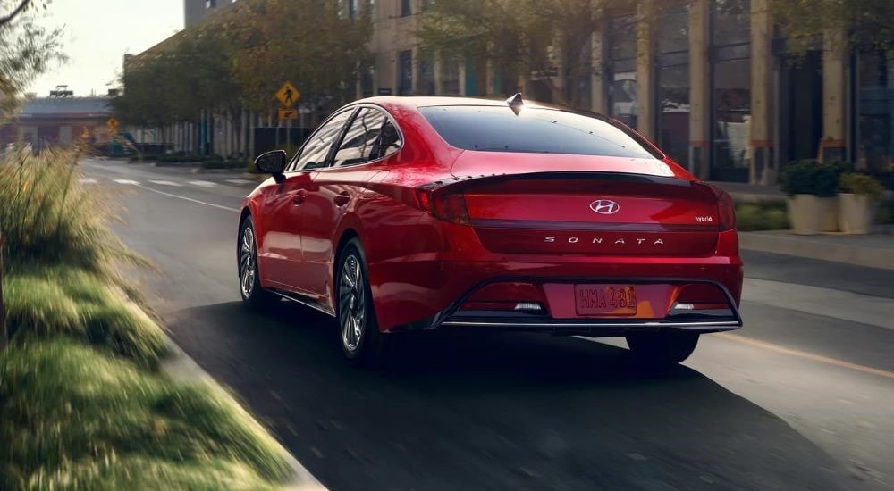 A red 2022 Hyundai Sonata Hybrid is shown from the rear driving on a city street.