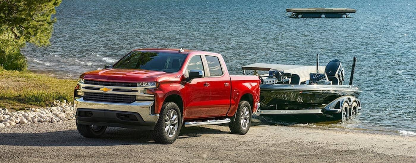A red 2022 Chevy Silverado 1500 LTD is shown towing a boat out of a lake.