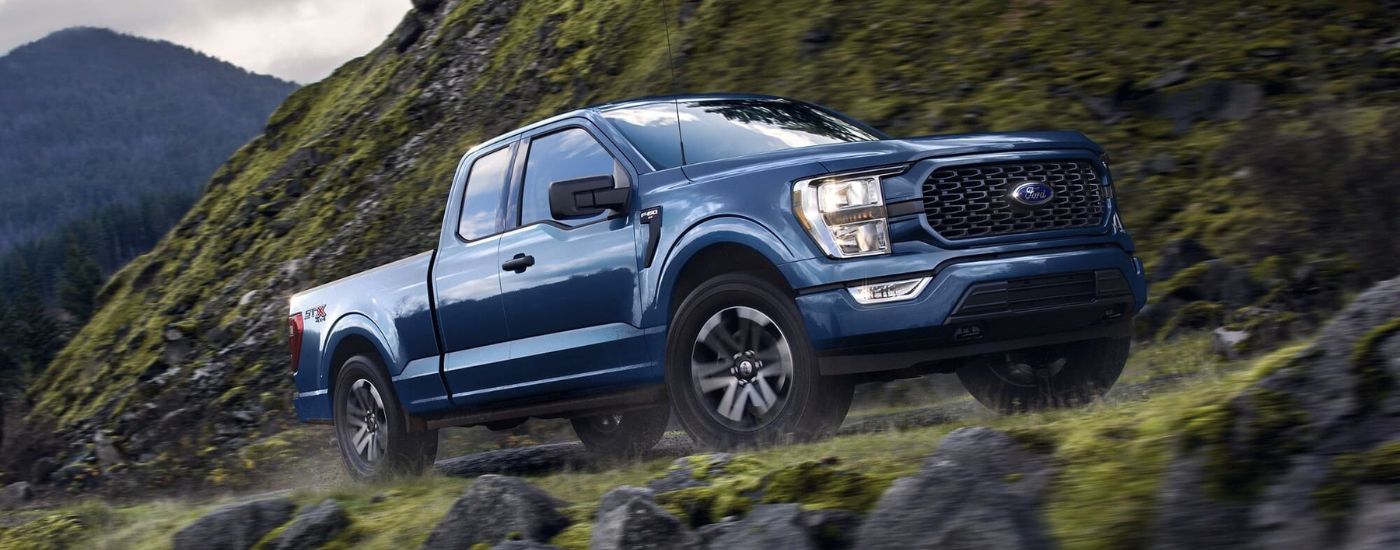 Blue 2023 Ford F-150 STX driving up a hill