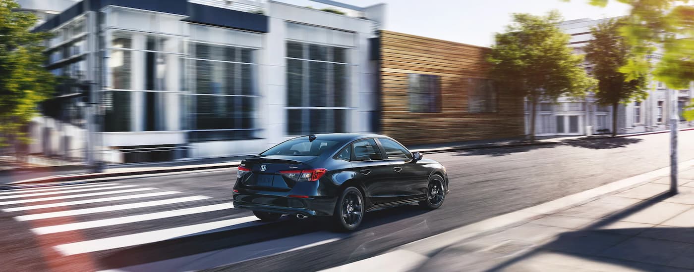 A black 2022 Honda Civic Sport is shown from a rear angle driving on a city street after leaving a used car dealership near Atlanta.