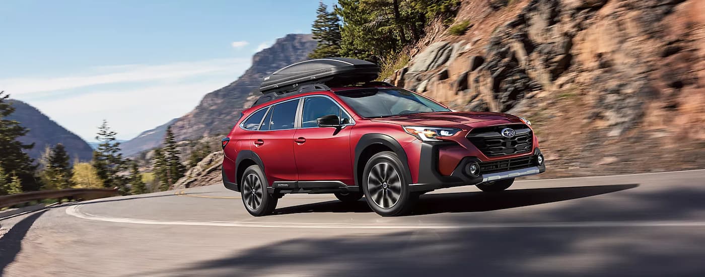 Red 2023 Subaru Outback driving on a winding road.