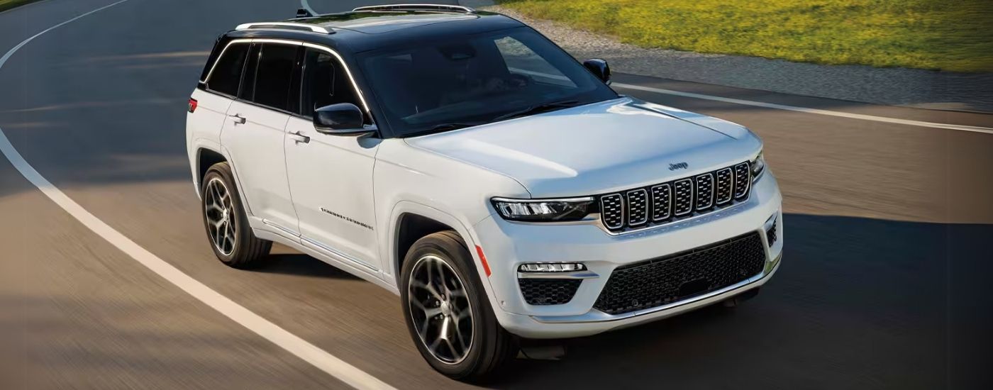White 2025 Jeep Grand Cherokee driving on a winding road