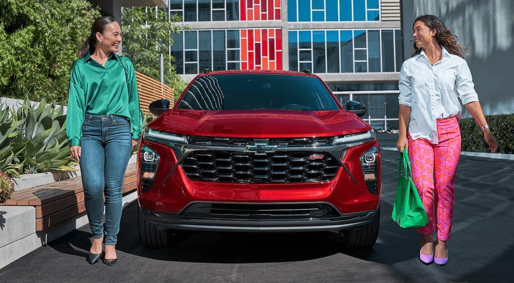 Two women walking by a red 2026 Chevy Trax