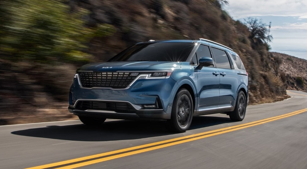 Blue 2024 Kia Carnival rounding a corner