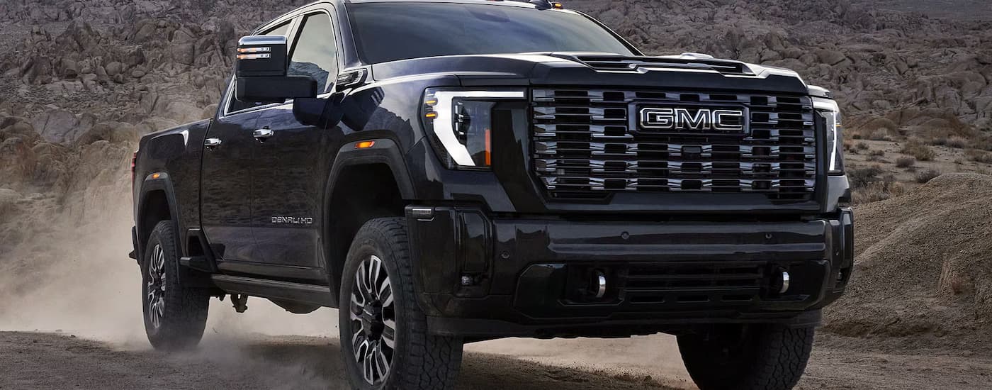 Black 2025 GMC Sierra 2500HD Denali off-roading on a dirt road.