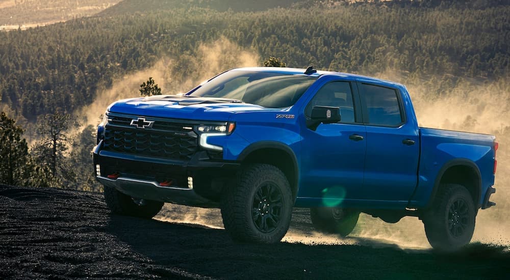 Blue 2026 Chevy Silverado 1500 driving up a dirt hill.