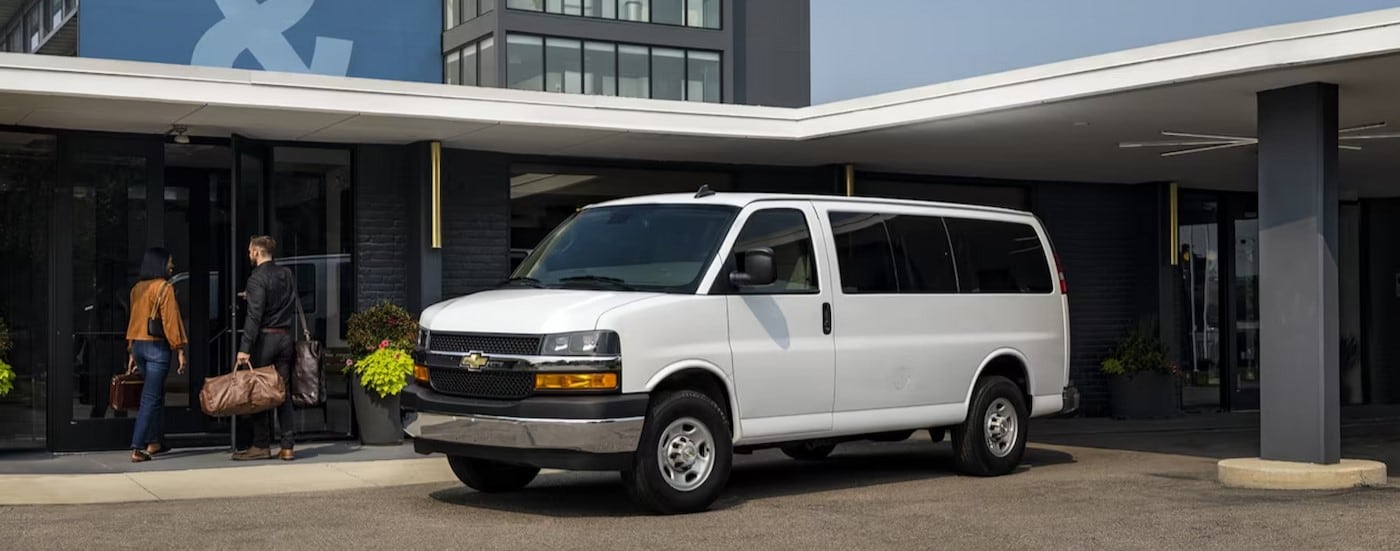 A white 2024 Chevy Express van is shown parked near a hotel.