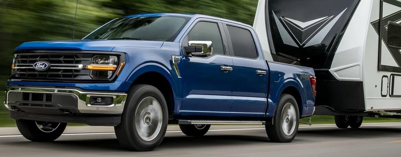 Blue 2024 Ford F-150 towing a camper trailer.