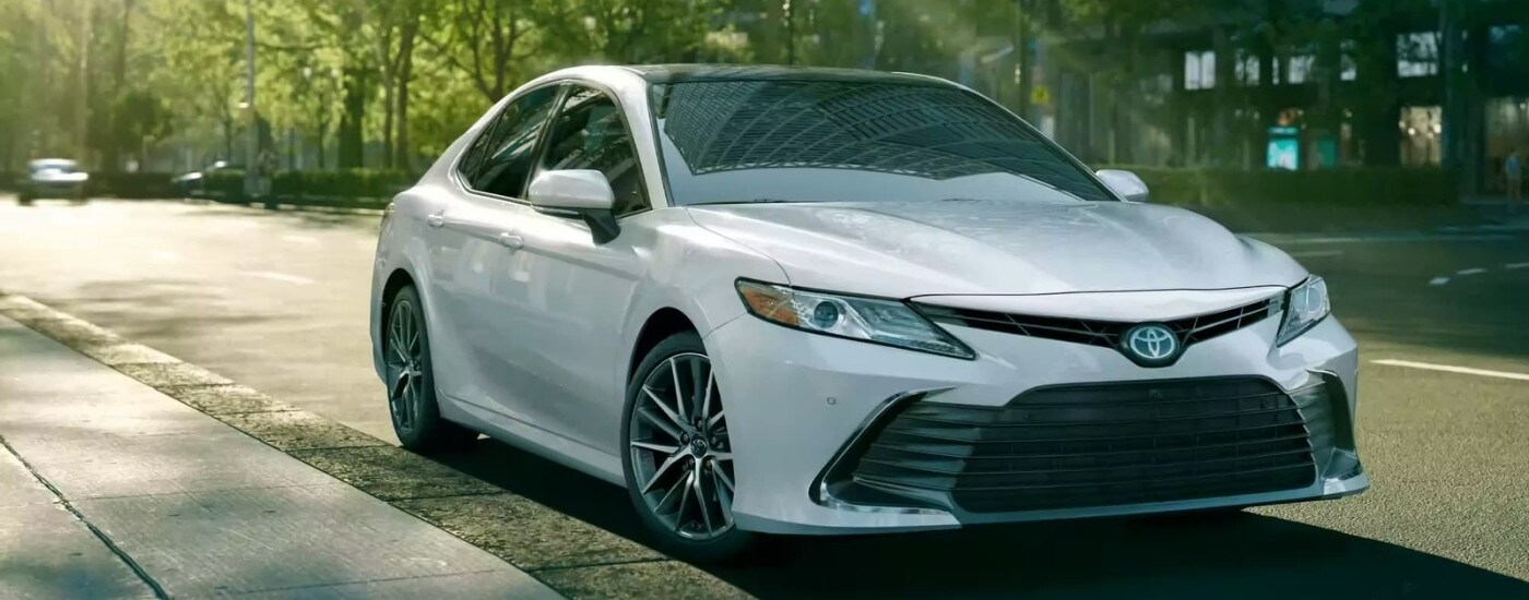 A white 2023 Toyota Camry parked on a tree-lined street.