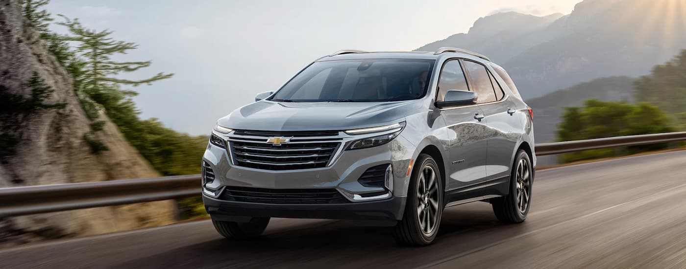 A grey 2023 Chevy Equinox is shown driving on a mountain highway.