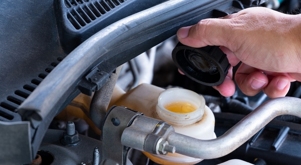 A close-up shows a person opening a brake fluid reservoir.