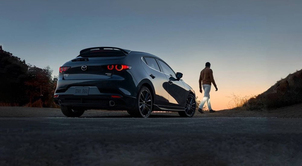 Rear view of a person walking from a parked black 2025 Mazda3.