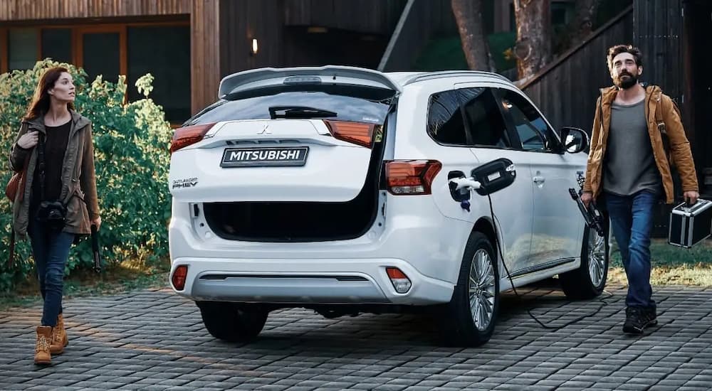 Two people walking away from a white 2024 Mitsubishi Outlander parked outside a SUV dealership near Raleigh.