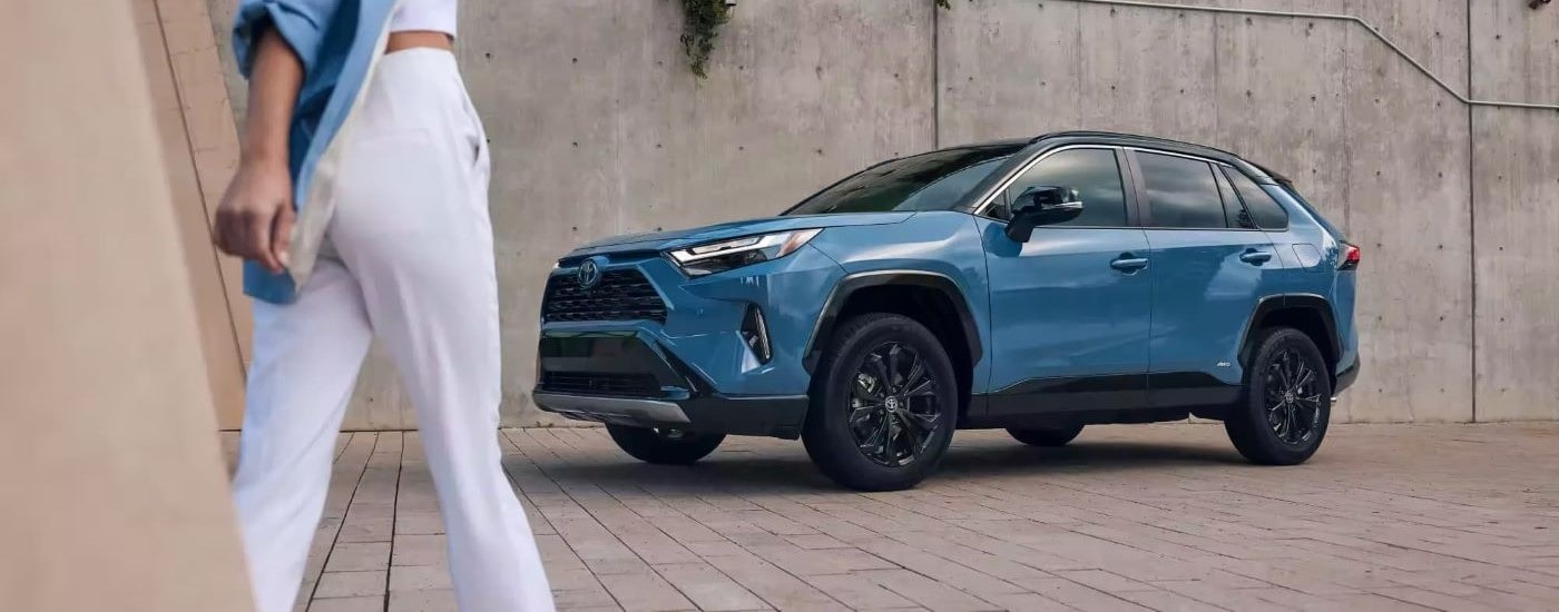 Blue 2023 Toyota RAV4 parked with the driver approaching