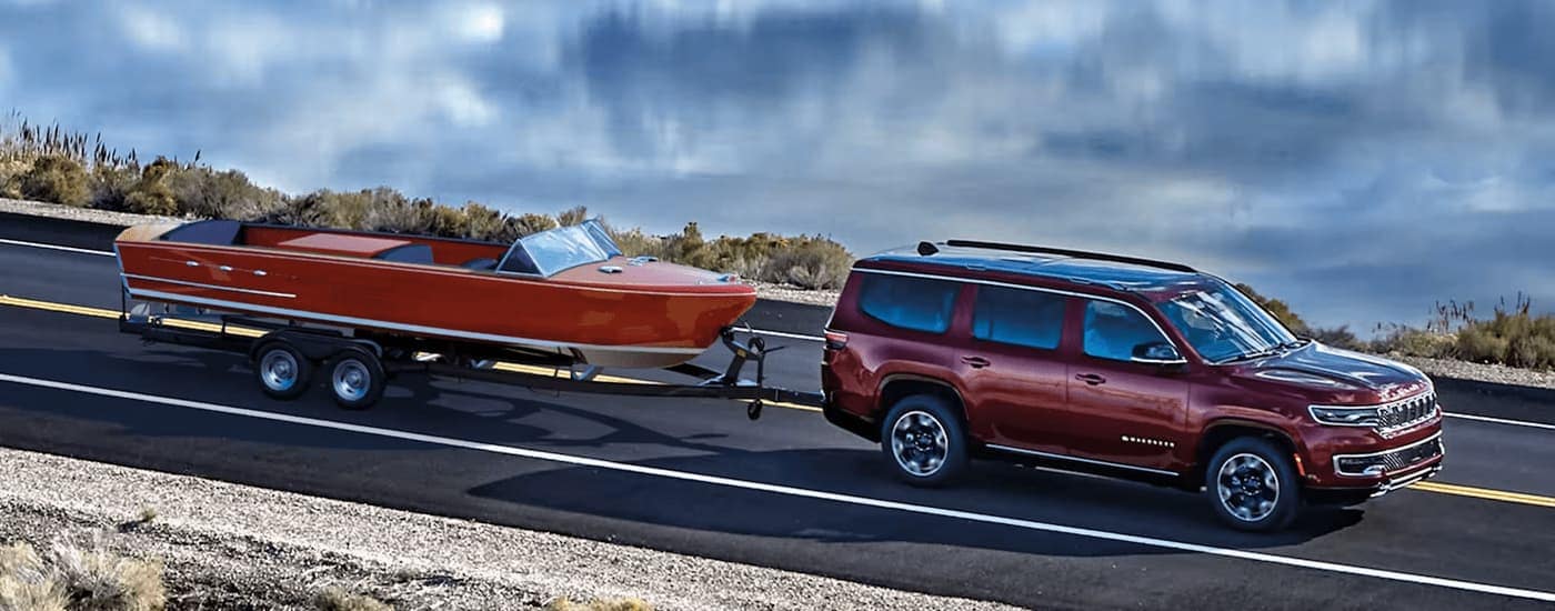 A red 2023 Jeep Wagoneer is towing a boat next to a lake.