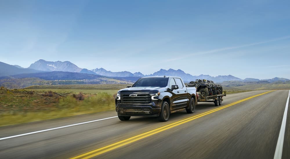 Black 2025 Chevy Silverado 1500 towing ATVs on a trailer