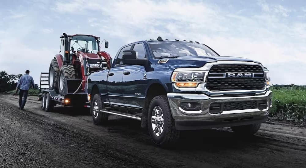 A blue 2024 Ram 2500 Laramie is shown towing a trailer off-road.