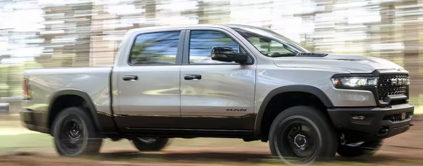 A white 2024 Ram 1500 driving through a forest from a truck dealership near Charleston.
