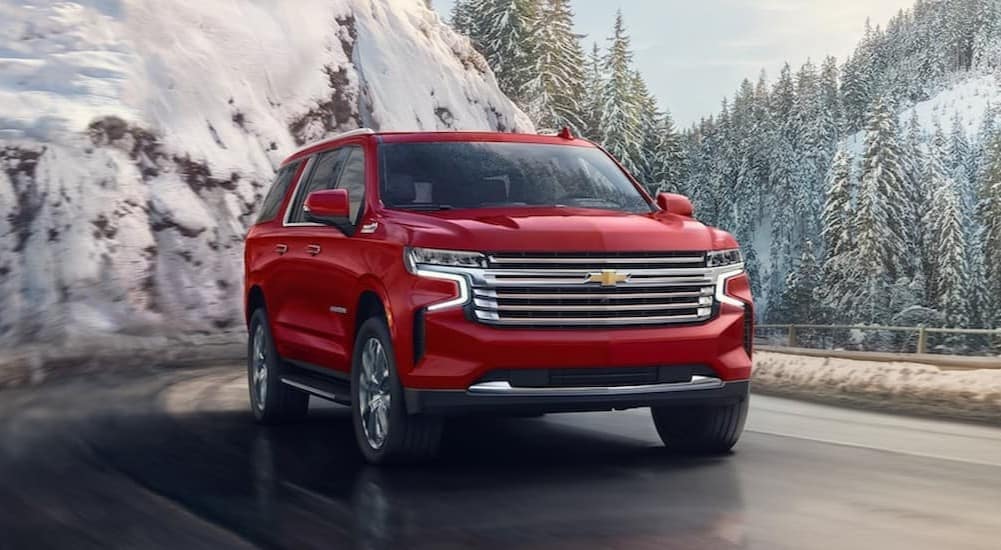 A red 2024 Chevy Suburban driving down a snowy mountain road.