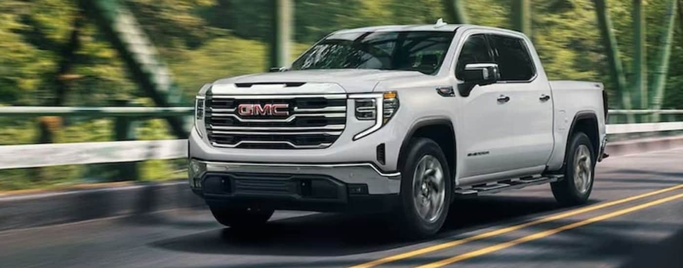 A white 2024 GMC Sierra 1500 is shown driving to view work trucks for sale in Raleigh.